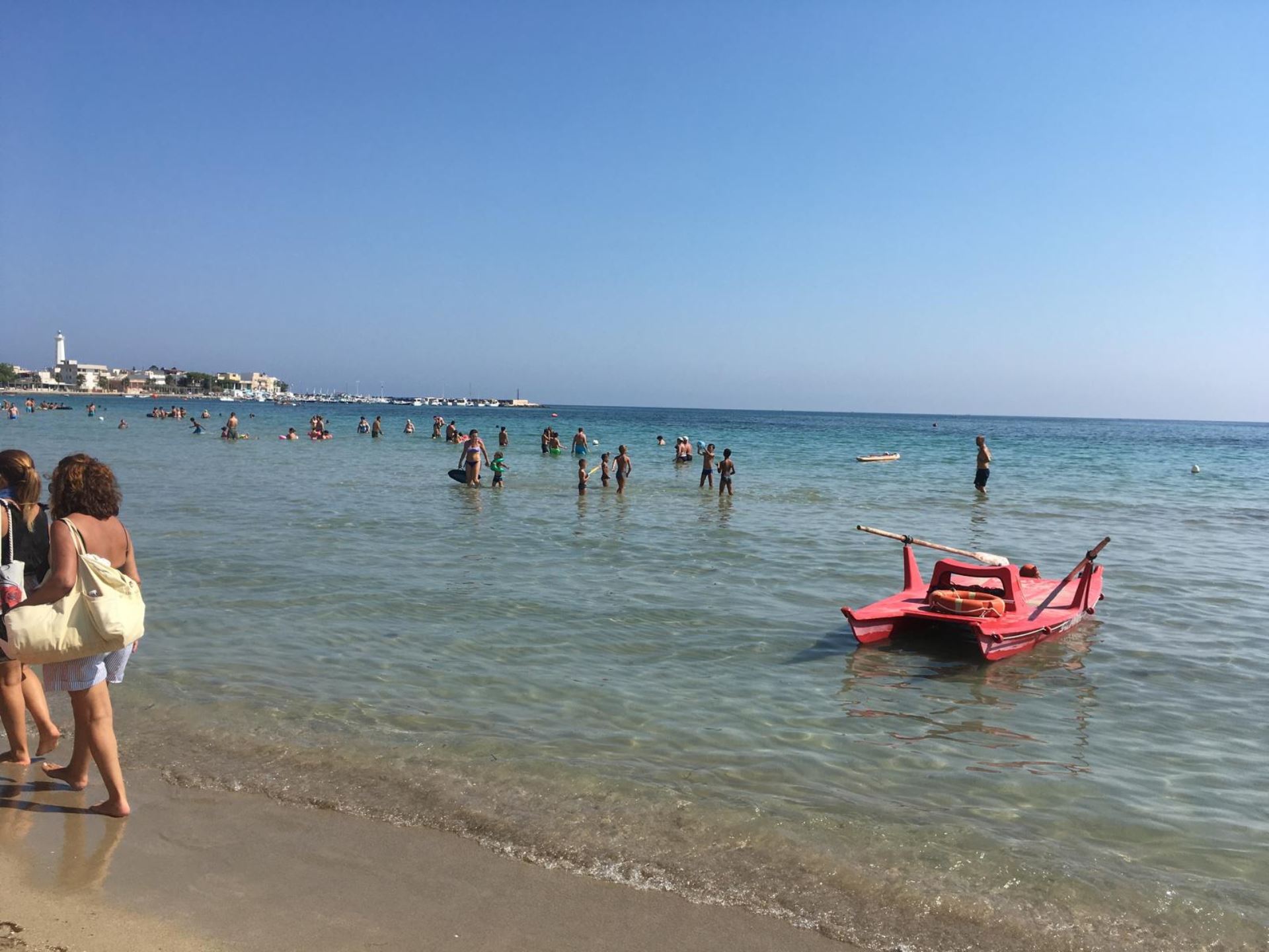 Spiaggia di Torre Canne con bagnanti e un pattino rosso, immersi nelle acque cristalline della Puglia.